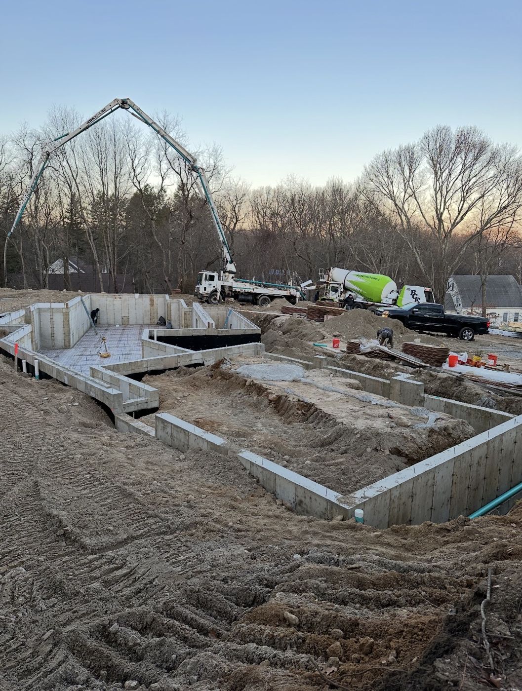Pump truck boom over a stripped residential foundation at dusk