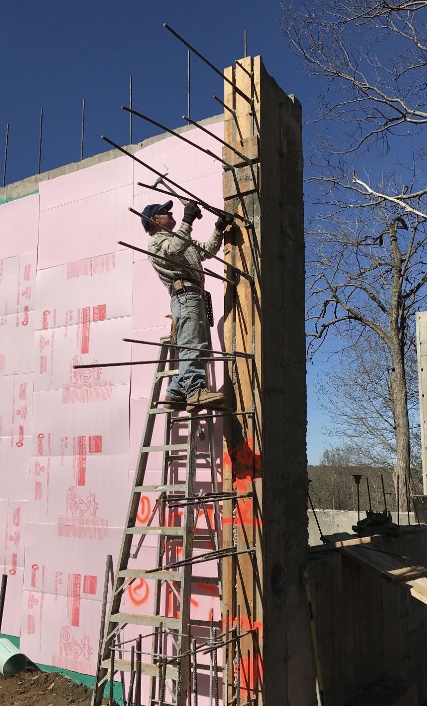 Crew member setting rebar at the end of a tall wall